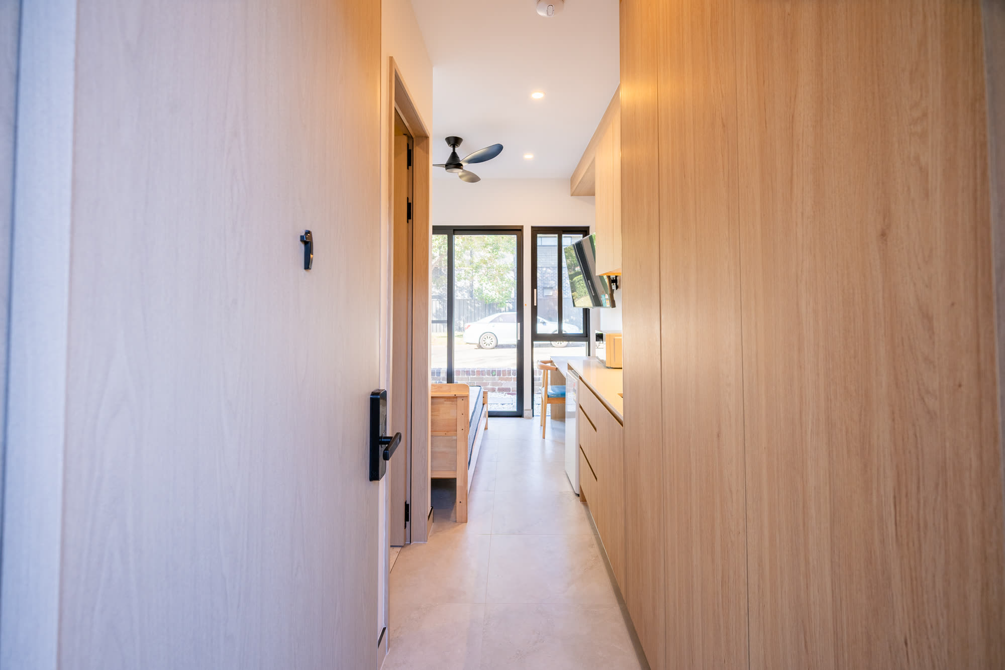 Internal corridor in a completed Auzzy Projects co-living home in Western Sydney, lined with full-height timber joinery, with a room door open to the shared living area beyond